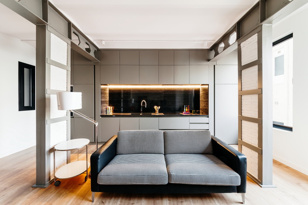 Photo of a mid-sized contemporary single-wall open plan kitchen in Other with flat-panel cabinets, grey cabinets, black splashback, medium hardwood floors, no island and black benchtop.