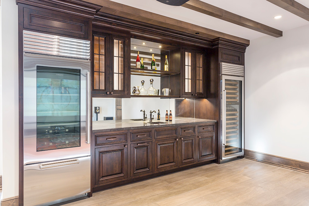 Photo of a large traditional single-wall wet bar in Phoenix with an undermount sink, raised-panel cabinets, dark wood cabinets, granite benchtops, light hardwood floors and beige floor.