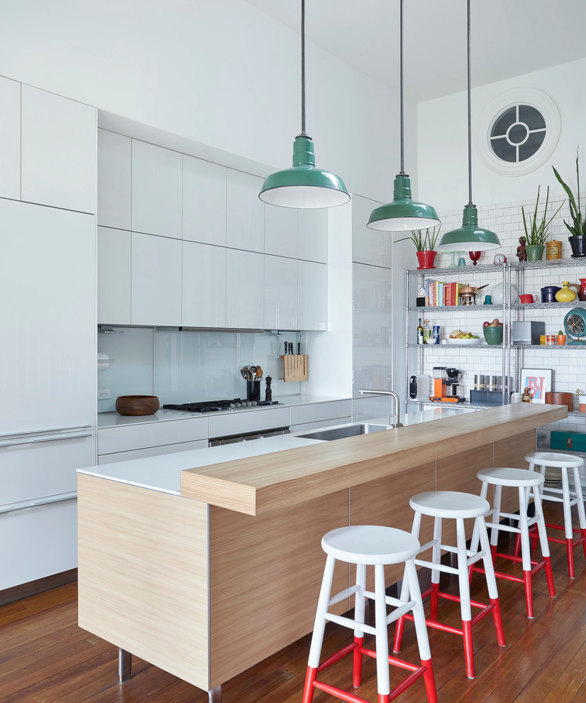 Design ideas for an eclectic galley kitchen in New York with with island, a single-bowl sink, flat-panel cabinets, white cabinets, white splashback, glass sheet splashback, stainless steel appliances, dark hardwood floors and brown floor.