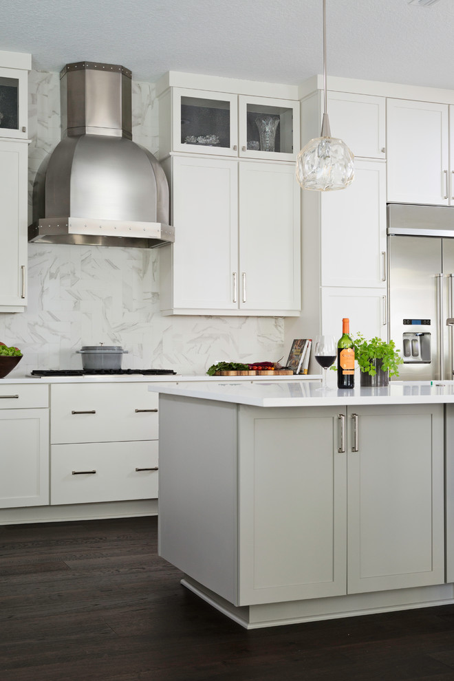 Inspiration for a mid-sized transitional l-shaped dark wood floor and brown floor eat-in kitchen remodel in Orlando with an undermount sink, shaker cabinets, white cabinets, solid surface countertops, white backsplash, stone slab backsplash, stainless steel appliances, an island and white countertops