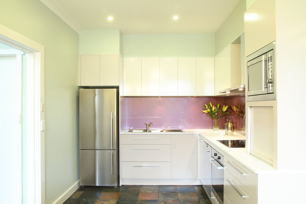 Photo of a mid-sized contemporary u-shaped separate kitchen in Sydney with a double-bowl sink, flat-panel cabinets, white cabinets, quartz benchtops, pink splashback, glass sheet splashback, stainless steel appliances and terra-cotta floors.