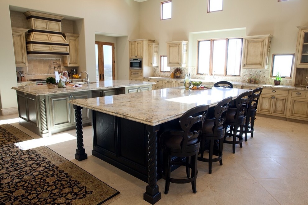 Photo of an expansive traditional u-shaped open plan kitchen in Phoenix with an undermount sink, raised-panel cabinets, black cabinets, granite benchtops, beige splashback, mosaic tile splashback, stainless steel appliances, limestone floors and multiple islands.
