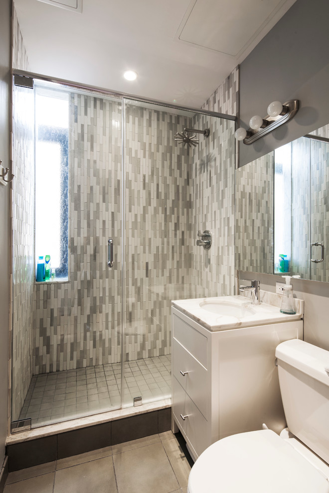This is an example of a small modern bathroom in New York with flat-panel cabinets, white cabinets, multi-coloured tile, grey walls, marble benchtops, a hinged shower door, an alcove shower, a one-piece toilet, pebble tile floors, an undermount sink, grey floor and white benchtops.