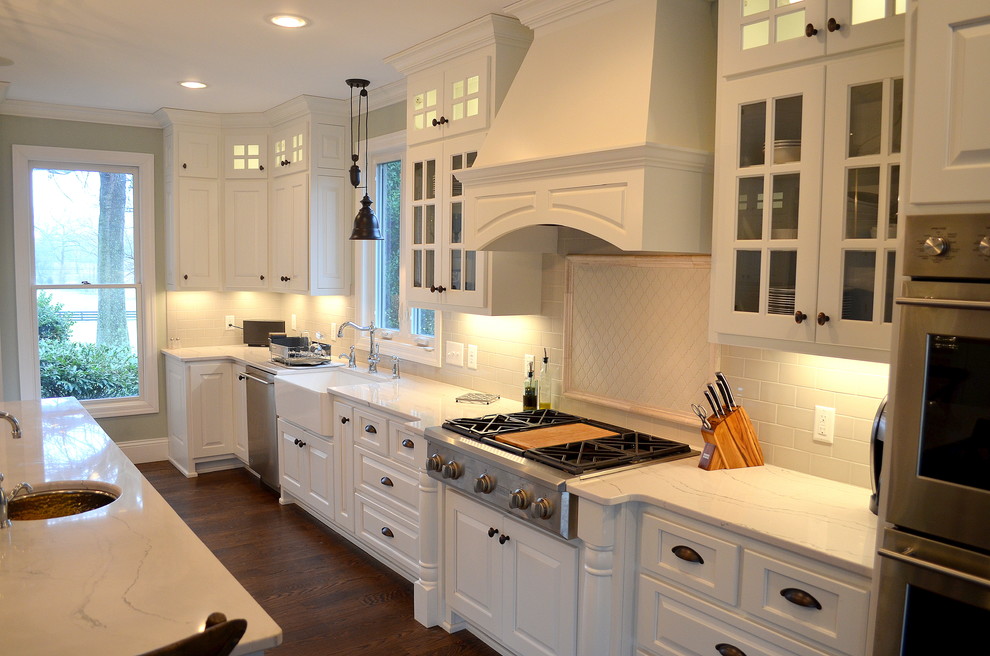 Inspiration for an expansive traditional l-shaped open plan kitchen in Nashville with a farmhouse sink, raised-panel cabinets, white cabinets, quartz benchtops, white splashback, ceramic splashback, stainless steel appliances, dark hardwood floors and with island.