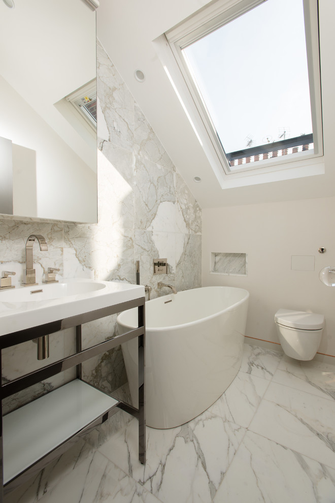 Photo of a contemporary bathroom in London with a console sink, a freestanding tub, a wall-mount toilet, marble floors, open cabinets, gray tile, white walls and marble.