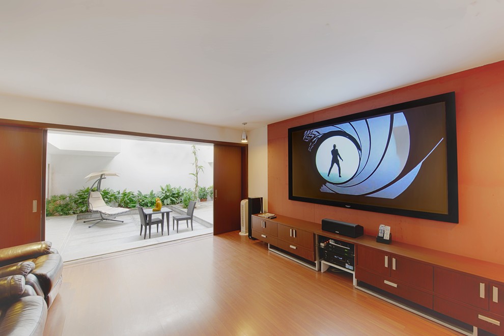 Mid-sized contemporary enclosed home theatre in Bengaluru with orange walls, laminate floors and a wall-mounted tv.