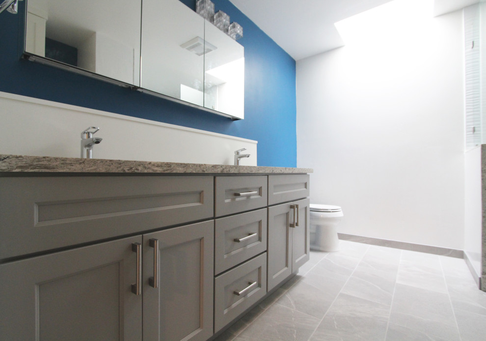 Example of a mid-sized transitional master white tile and porcelain tile porcelain tile, gray floor and double-sink walk-in shower design with shaker cabinets, gray cabinets, a two-piece toilet, blue walls, an undermount sink, quartz countertops, multicolored countertops, a niche and a built-in vanity