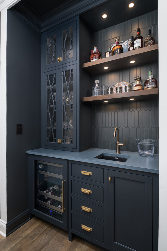 Foto på en liten vintage svarta linjär hemmabar med vask, med en undermonterad diskho, skåp i shakerstil, blå skåp, bänkskiva i kvarts, svart stänkskydd, stänkskydd i porslinskakel, mellanmörkt trägolv och brunt golv