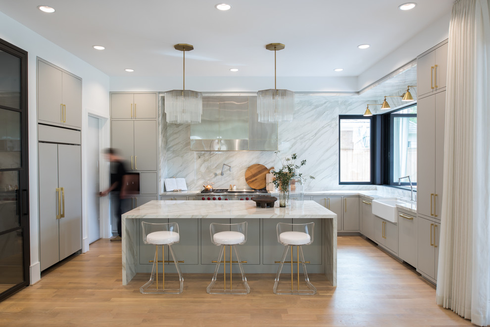 Photo of a large contemporary u-shaped kitchen in Houston with a farmhouse sink, flat-panel cabinets, grey cabinets, marble benchtops, white splashback, marble splashback, stainless steel appliances, light hardwood floors, with island, white benchtop and beige floor.