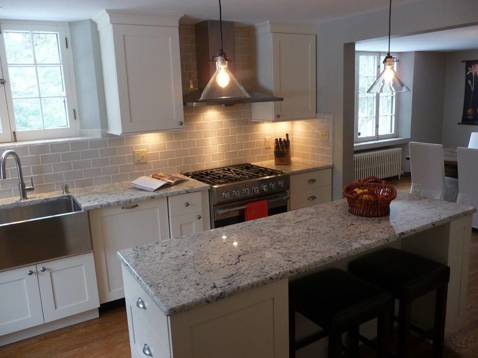 Example of a large transitional u-shaped light wood floor eat-in kitchen design in Milwaukee with a farmhouse sink, recessed-panel cabinets, white cabinets, granite countertops, gray backsplash, subway tile backsplash, stainless steel appliances and an island