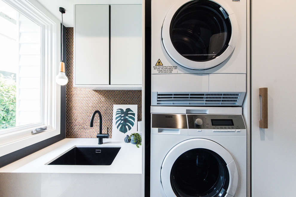Mid-sized contemporary single-wall dedicated laundry room in Melbourne with an undermount sink, flat-panel cabinets, white cabinets, quartz benchtops, black walls and a stacked washer and dryer.
