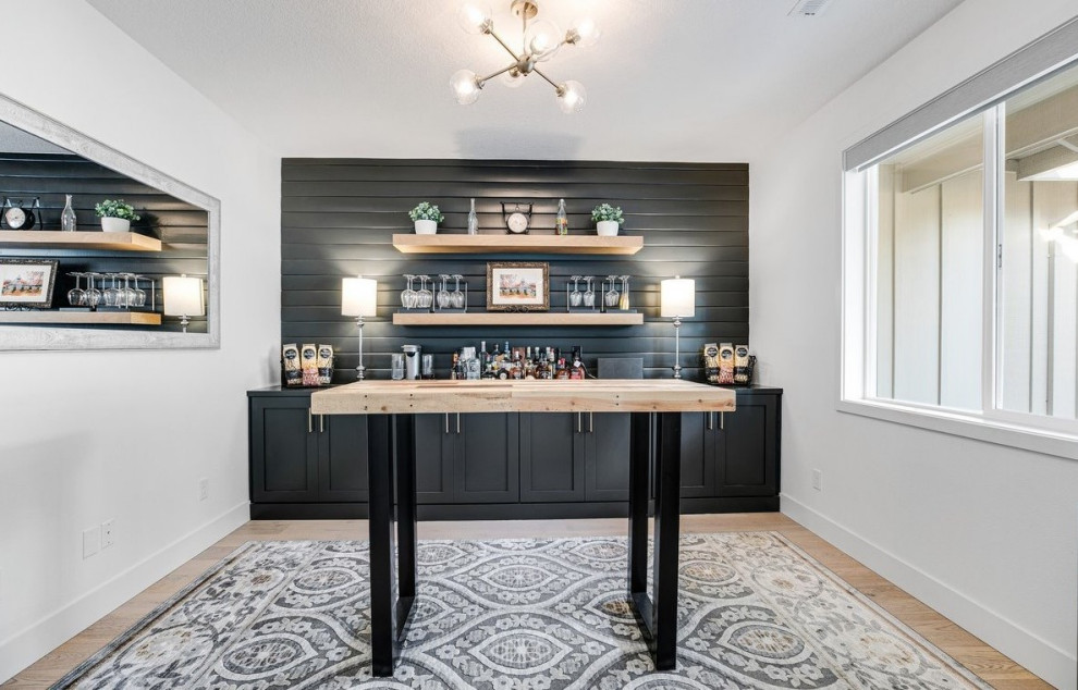 Photo of a small country single-wall home bar in Portland with recessed-panel cabinets, black cabinets, wood benchtops, black splashback, light hardwood floors and black benchtop.