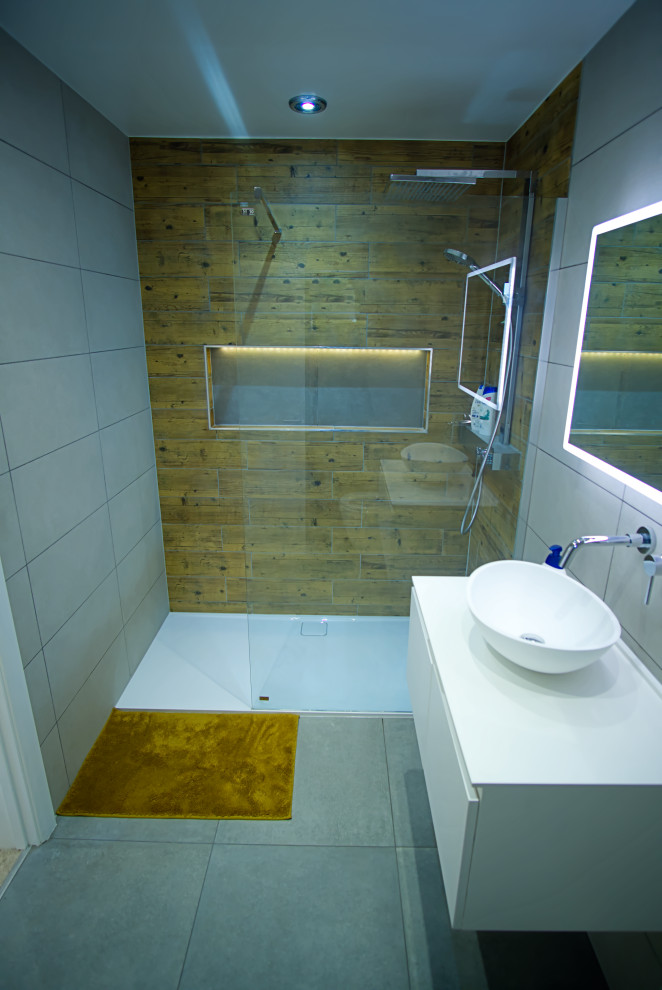 This is an example of a mid-sized modern master bathroom in Hertfordshire with flat-panel cabinets, white cabinets, a drop-in tub, an open shower, a one-piece toilet, gray tile, limestone, grey walls, limestone floors, a wall-mount sink, grey floor, a sliding shower screen, white benchtops, a niche, a single vanity and a built-in vanity.