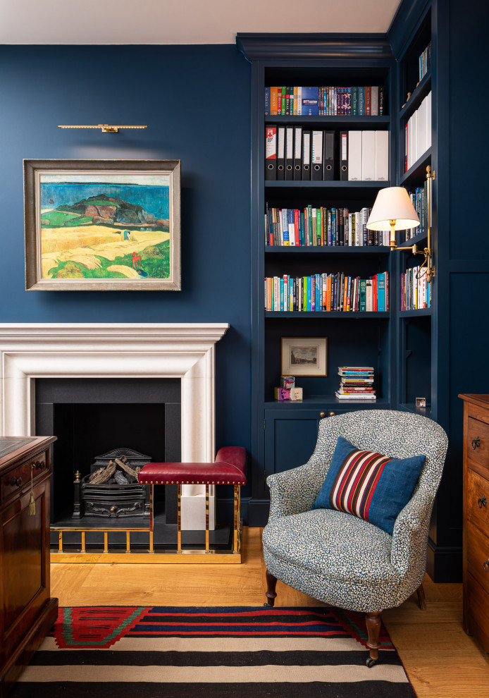 Inspiration for a mid-sized traditional study room in London with blue walls, medium hardwood floors, a standard fireplace and a freestanding desk.