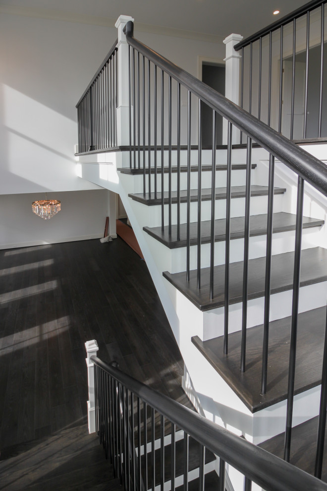 На фото: большая деревянная лестница на больцах в стиле неоклассика (современная классика) с деревянными ступенями, перилами из смешанных материалов и панелями на части стены с