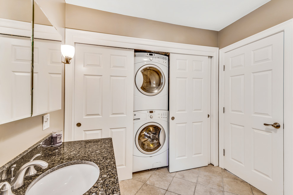 This is an example of a mid-sized traditional single-wall laundry cupboard in Boston with an undermount sink, brown walls, ceramic floors, a stacked washer and dryer and brown floor.