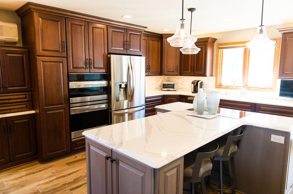 Example of a transitional ceramic tile and brown floor eat-in kitchen design with brown cabinets, quartzite countertops, beige backsplash, ceramic backsplash, stainless steel appliances, an island and white countertops