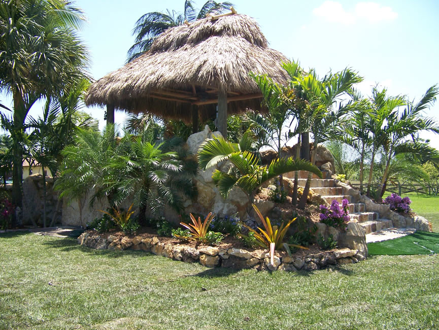 This is an example of a large tropical backyard patio in Miami with a gazebo/cabana and natural stone pavers.