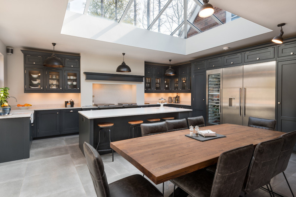 Photo of a large transitional u-shaped eat-in kitchen in Other with a farmhouse sink, shaker cabinets, black cabinets, white splashback, stainless steel appliances, with island, grey floor and white benchtop.