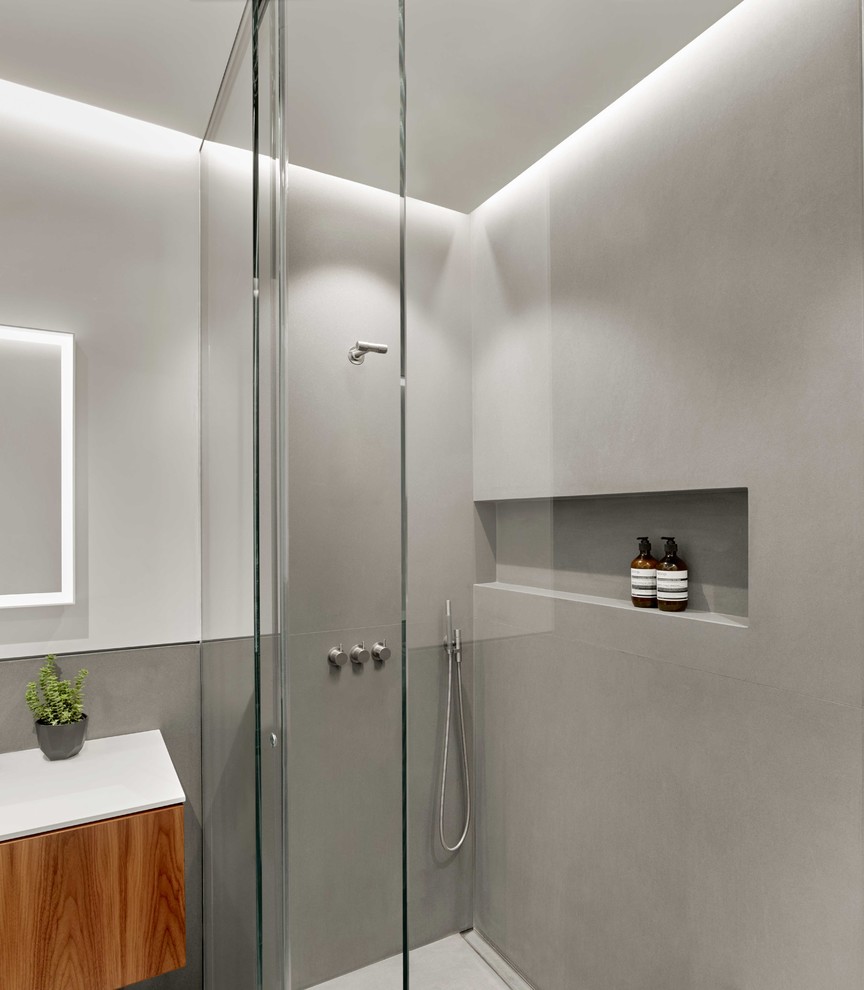 This is an example of a mid-sized modern master bathroom in San Francisco with furniture-like cabinets, medium wood cabinets, a drop-in tub, a curbless shower, a wall-mount toilet, stone slab, grey walls, limestone floors, an integrated sink, solid surface benchtops, grey floor and a sliding shower screen.