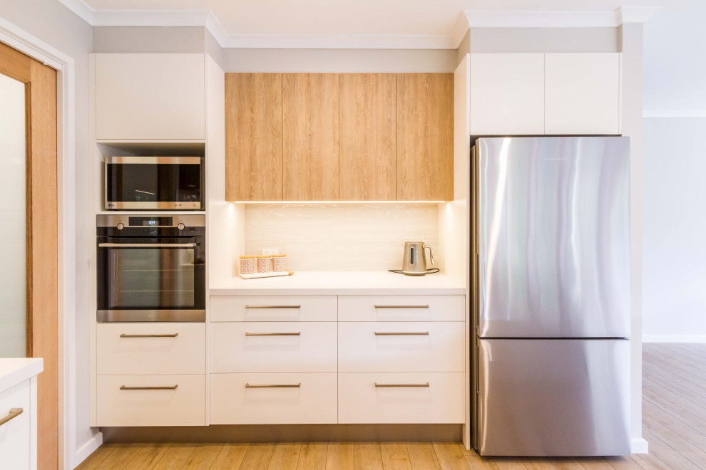 Inspiration for a mid-sized scandinavian u-shaped open plan kitchen in Melbourne with a double-bowl sink, flat-panel cabinets, white cabinets, quartz benchtops, white splashback, porcelain splashback, stainless steel appliances, medium hardwood floors, a peninsula, beige floor and white benchtop.