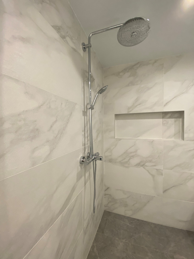 На фото: большая главная ванная комната в скандинавском стиле с душевой комнатой, белой плиткой, керамической плиткой, белыми стенами, полом из керамической плитки, душем с распашными дверями, нишей и серым полом