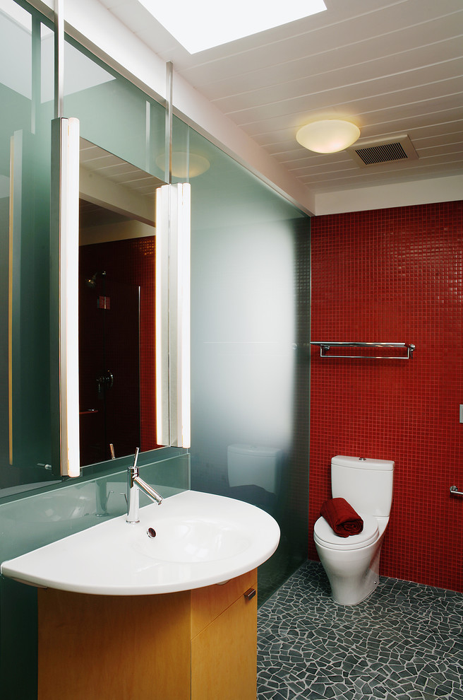 This is an example of a small contemporary 3/4 bathroom in San Francisco with flat-panel cabinets, light wood cabinets, red tile, red walls, glass tile, pebble tile floors, an integrated sink and black floor.