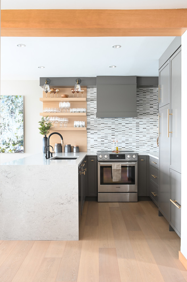 Contemporary u-shaped kitchen in Vancouver with an undermount sink, shaker cabinets, grey cabinets, white splashback, mosaic tile splashback, light hardwood floors, a peninsula, beige floor and white benchtop.