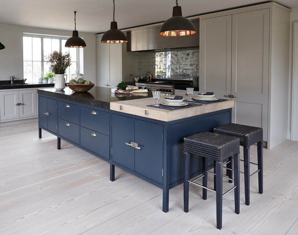 Inspiration for a mid-sized contemporary l-shaped open plan kitchen in London with an integrated sink, flat-panel cabinets, blue cabinets, marble benchtops, metallic splashback, mirror splashback, stainless steel appliances, light hardwood floors, with island, brown floor and black benchtop.