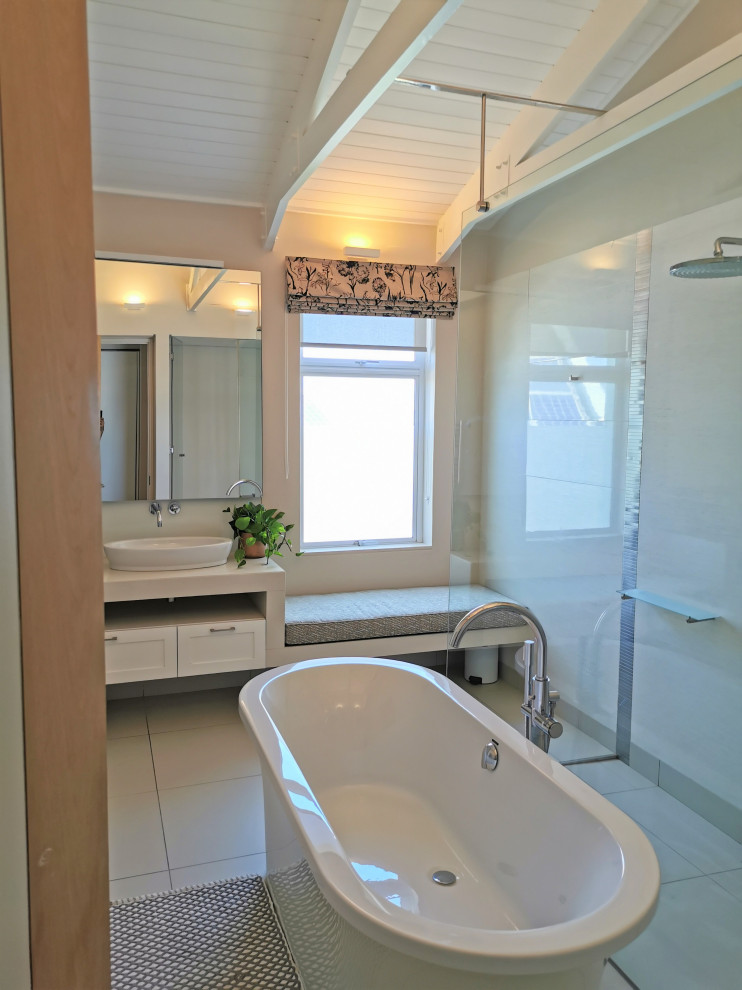 This is an example of a medium sized beach style bathroom with a freestanding bath, a wall mounted toilet, white walls, a sliding door, an enclosed toilet, a single sink, a built in vanity unit and exposed beams.