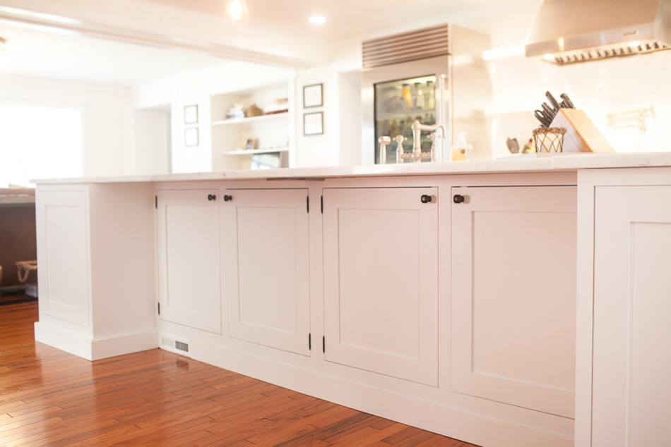 Example of a mid-sized transitional medium tone wood floor eat-in kitchen design in St Louis with a farmhouse sink, flat-panel cabinets, white cabinets, white backsplash, subway tile backsplash, stainless steel appliances and an island