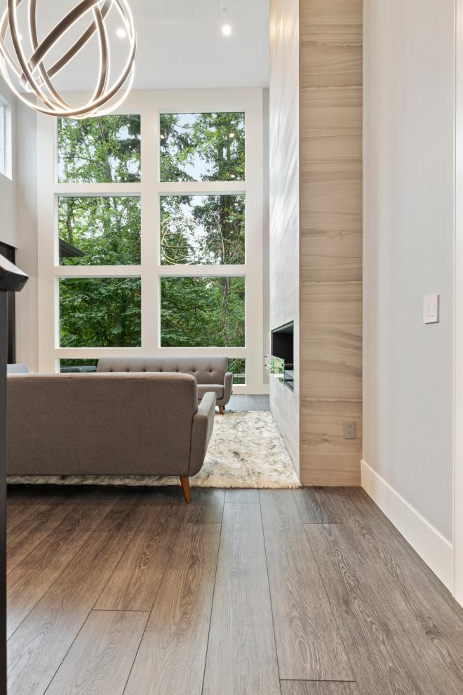 Cette image montre un grand salon minimaliste ouvert avec une salle de réception, un mur gris, un sol en vinyl, une cheminée standard, un manteau de cheminée en pierre, un sol gris et un plafond voûté.
