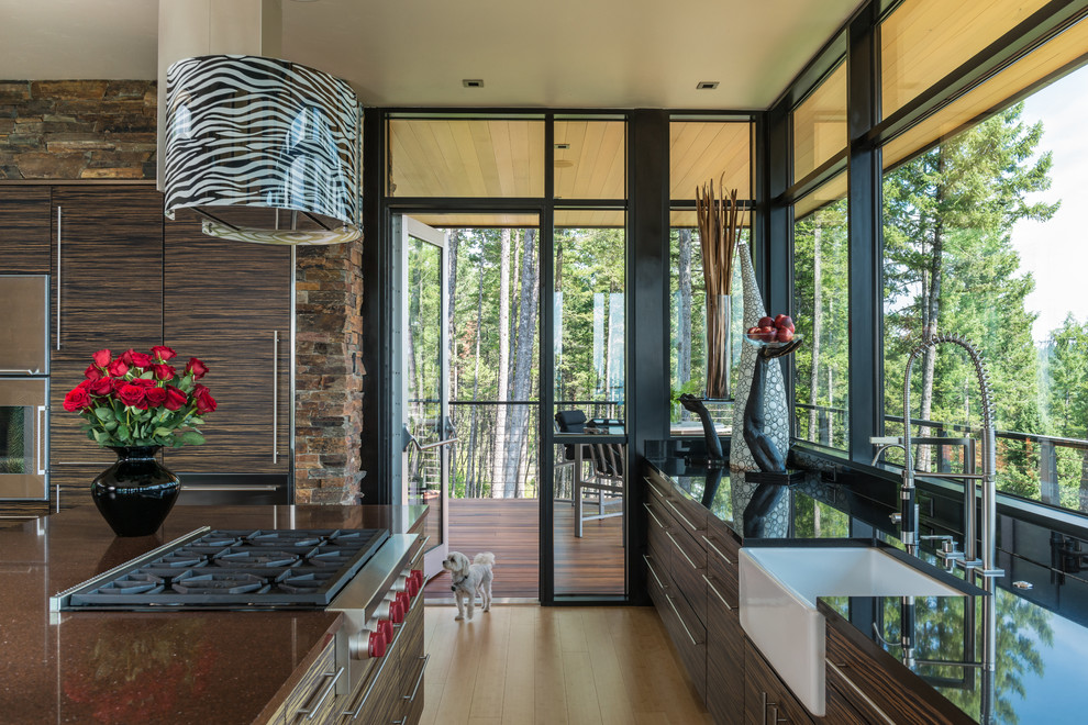 This is an example of a contemporary kitchen in Other with a farmhouse sink, flat-panel cabinets, dark wood cabinets, stainless steel appliances, light hardwood floors and with island.