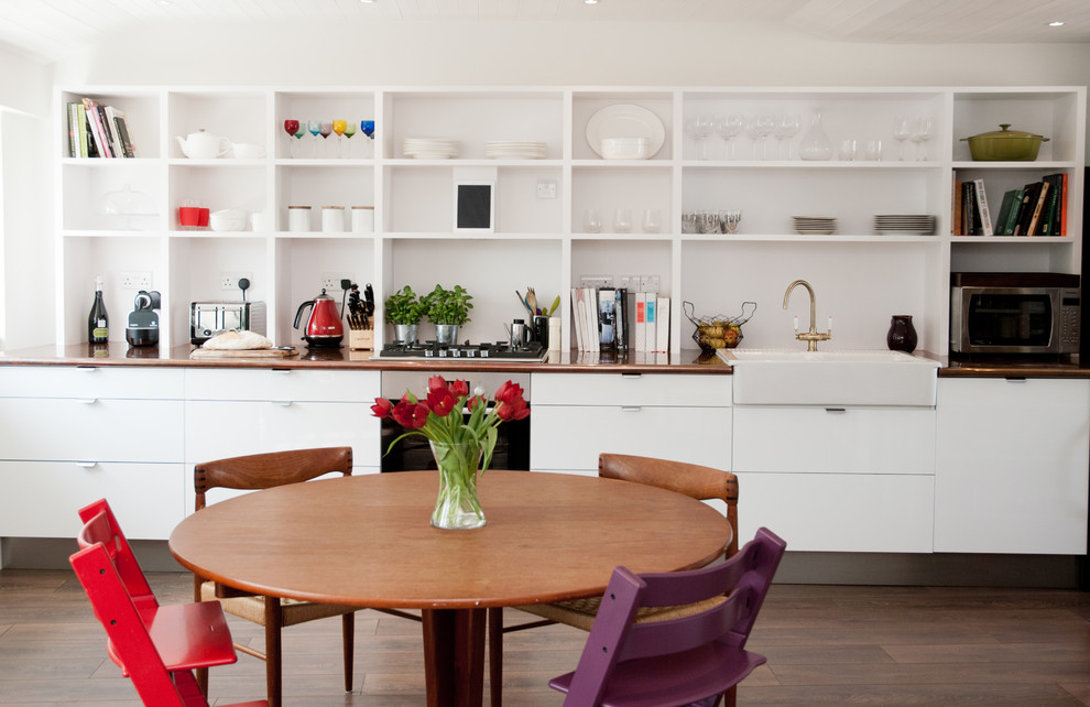 This is an example of a contemporary galley eat-in kitchen in London with a farmhouse sink, open cabinets, white cabinets and medium hardwood floors.