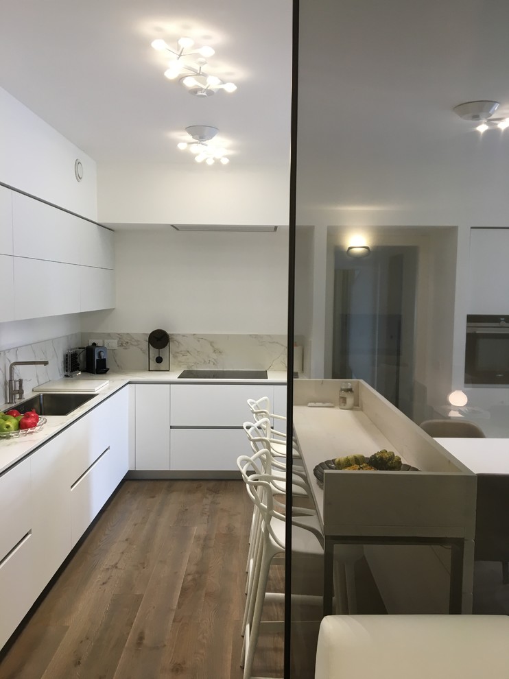 This is an example of a mid-sized modern eat-in kitchen in Milan with flat-panel cabinets, white cabinets, with island and white benchtop.