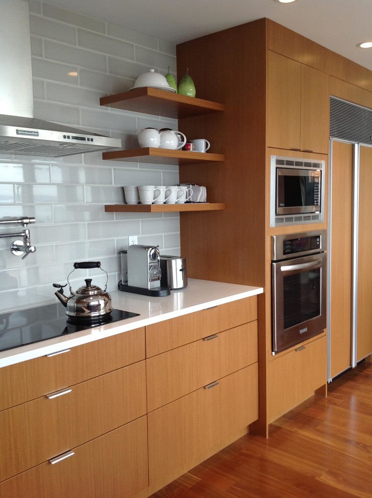 Photo of a contemporary kitchen in Vancouver with flat-panel cabinets, light wood cabinets, quartz benchtops, grey splashback, subway tile splashback, stainless steel appliances and medium hardwood floors.