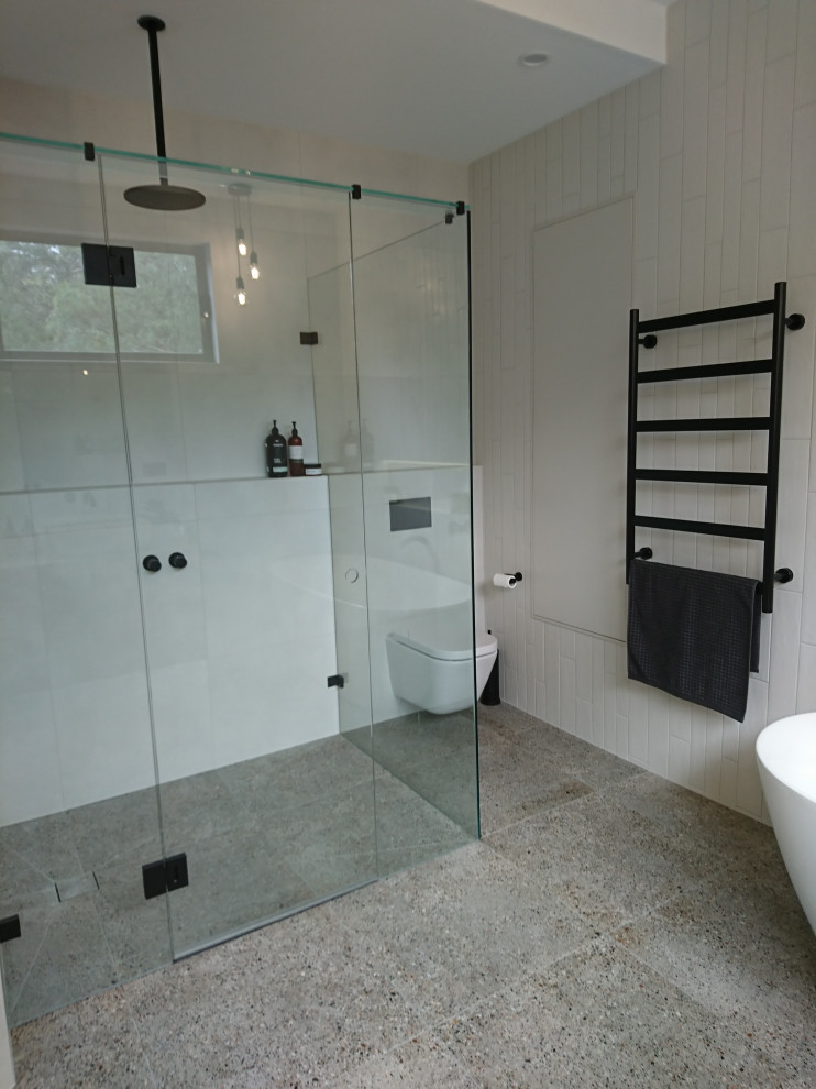 Design ideas for a large modern bathroom in Melbourne with flat-panel cabinets, medium wood cabinets, a freestanding bath, a one-piece toilet, white tiles, ceramic tiles, white walls, terrazzo flooring, a vessel sink, engineered stone worktops, grey floors, a hinged door, a wall niche, double sinks, a floating vanity unit, a vaulted ceiling and grey worktops.