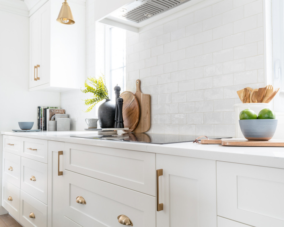 Example of a large transitional l-shaped medium tone wood floor and brown floor eat-in kitchen design with a triple-bowl sink, shaker cabinets, white cabinets, quartz countertops, white backsplash, subway tile backsplash, stainless steel appliances, an island and white countertops