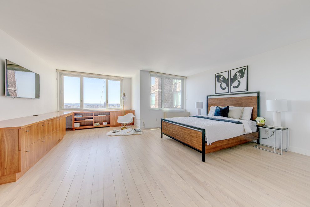 Expansive midcentury master bedroom in New York with white walls, light hardwood floors, no fireplace and brown floor.