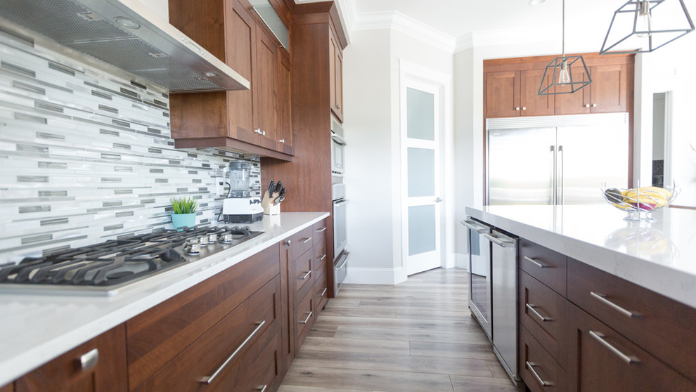 Open concept kitchen - transitional l-shaped beige floor open concept kitchen idea with a farmhouse sink, recessed-panel cabinets, medium tone wood cabinets, gray backsplash, mosaic tile backsplash, stainless steel appliances and an island