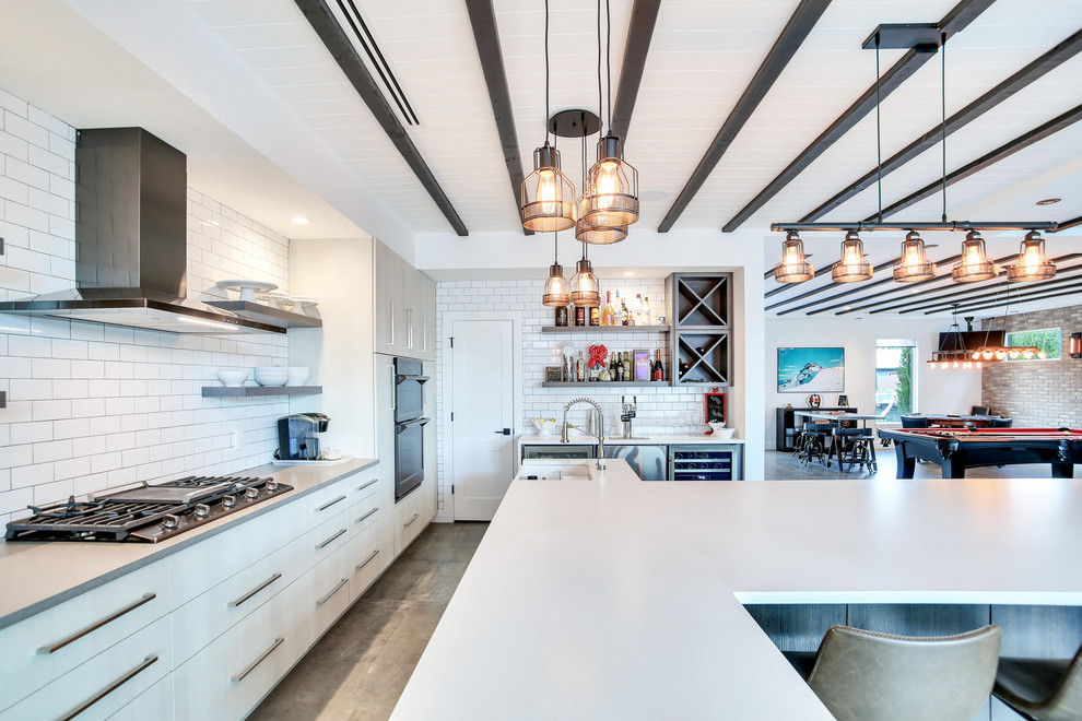 This is an example of a mid-sized industrial single-wall open plan kitchen in Tampa with a farmhouse sink, shaker cabinets, white cabinets, white splashback, subway tile splashback, stainless steel appliances, cement tiles, with island, grey floor and white benchtop.