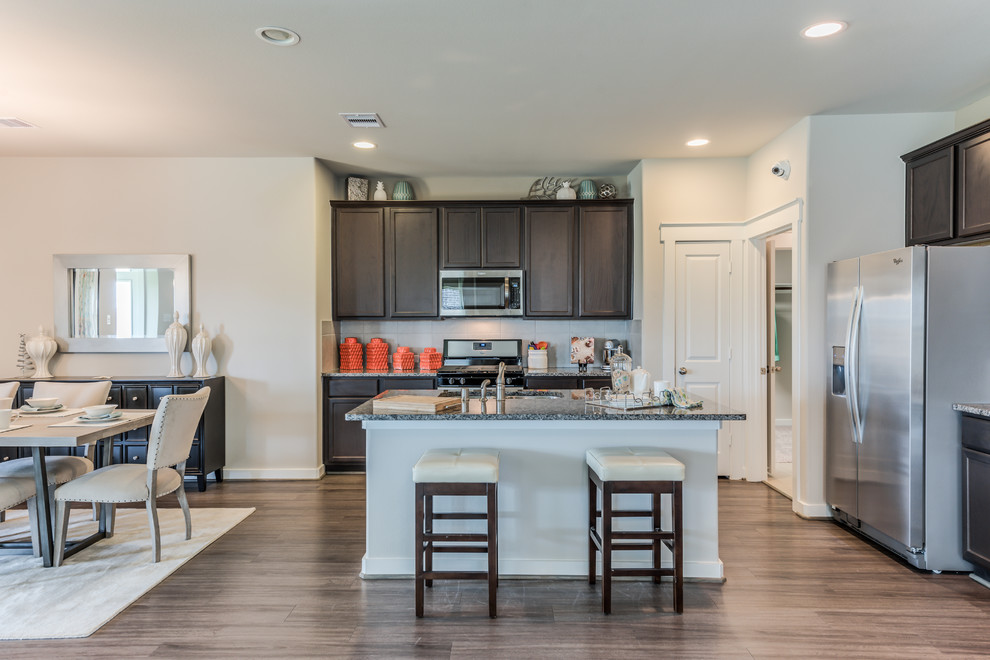 Mid-sized contemporary l-shaped eat-in kitchen in Houston with a double-bowl sink, raised-panel cabinets, dark wood cabinets, granite benchtops, beige splashback, ceramic splashback, stainless steel appliances, dark hardwood floors, with island, brown floor and brown benchtop.