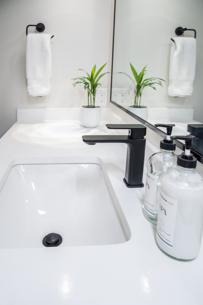 This is an example of a mid-sized transitional 3/4 bathroom in Edmonton with shaker cabinets, grey cabinets, an alcove tub, a shower/bathtub combo, a one-piece toilet, black and white tile, porcelain tile, grey walls, porcelain floors, an undermount sink, engineered quartz benchtops, black floor, a hinged shower door, white benchtops, a niche, a single vanity and a built-in vanity.