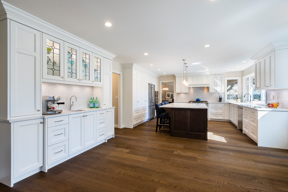 Inspiration for a large transitional u-shaped medium tone wood floor and brown floor eat-in kitchen remodel in Vancouver with an undermount sink, recessed-panel cabinets, white cabinets, quartz countertops, white backsplash, mosaic tile backsplash, stainless steel appliances and an island