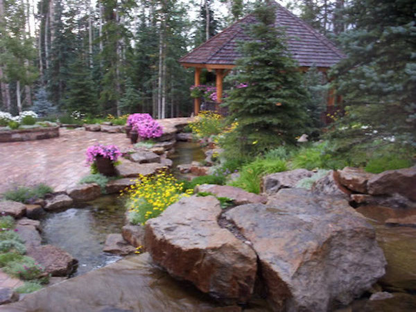 Photo of a huge rustic full sun backyard brick water fountain landscape in Denver.