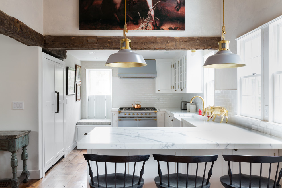 This is an example of a country u-shaped eat-in kitchen in Boston with a farmhouse sink, recessed-panel cabinets, white cabinets, white splashback, subway tile splashback, panelled appliances, medium hardwood floors, a peninsula and brown floor.