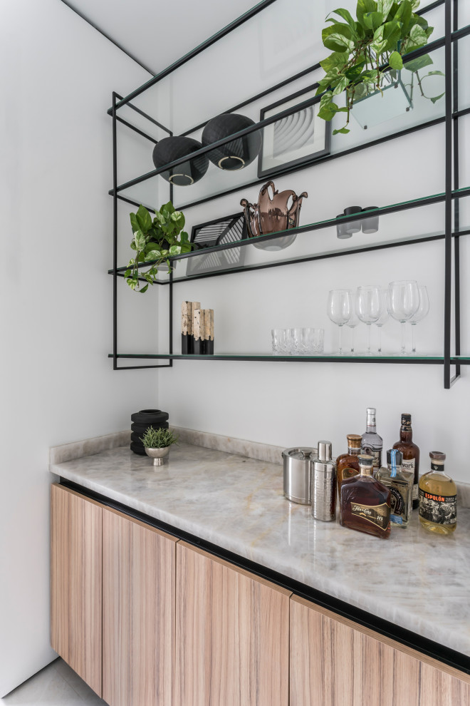 Design ideas for a medium sized contemporary single-wall dry bar in Miami with no sink, flat-panel cabinets, light wood cabinets, onyx worktops, beige splashback, marble splashback, ceramic flooring, grey floors and beige worktops.