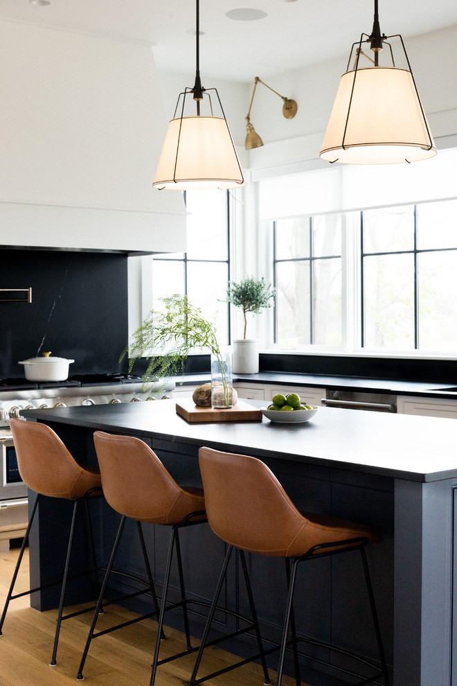 This is an example of a large transitional u-shaped open plan kitchen in Toronto with an undermount sink, recessed-panel cabinets, white cabinets, limestone benchtops, black splashback, limestone splashback, stainless steel appliances, light hardwood floors, with island, brown floor and black benchtop.