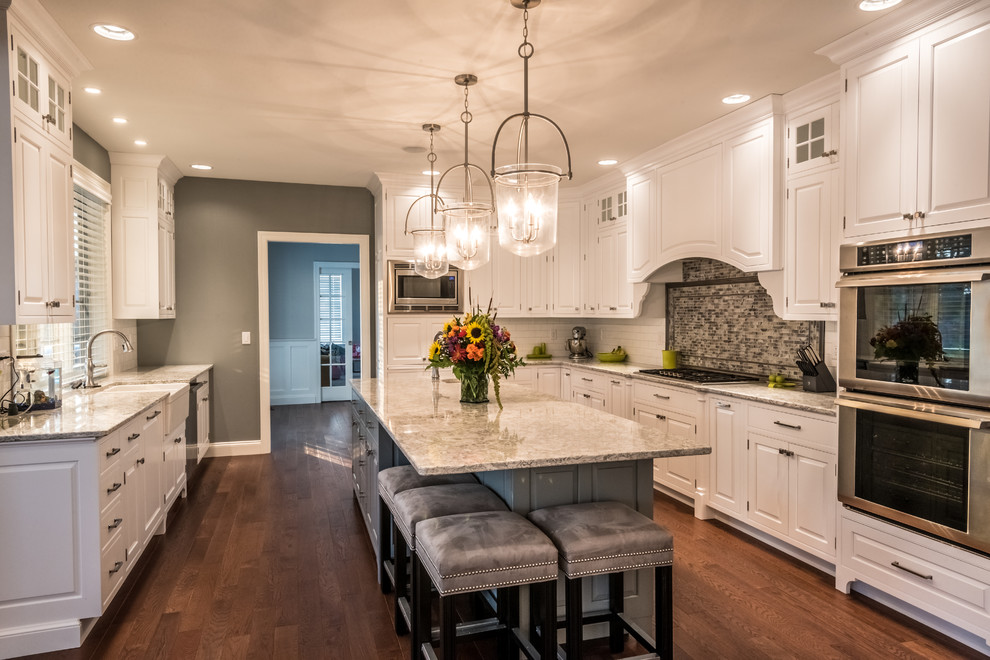 Large transitional galley medium tone wood floor eat-in kitchen photo with a farmhouse sink, beaded inset cabinets, white cabinets, granite countertops, white backsplash, mosaic tile backsplash, stainless steel appliances and an island