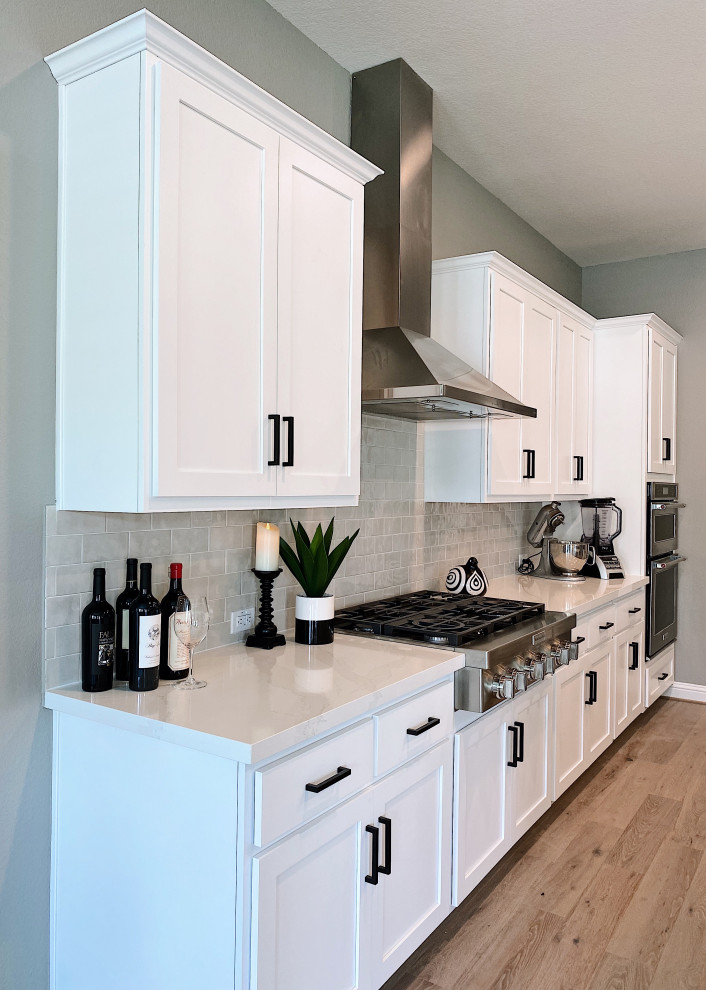 Contemporary single-wall kitchen/diner in Austin with a built-in sink, shaker cabinets, white cabinets, quartz worktops, beige splashback, stainless steel appliances, an island, beige floors and white worktops.
